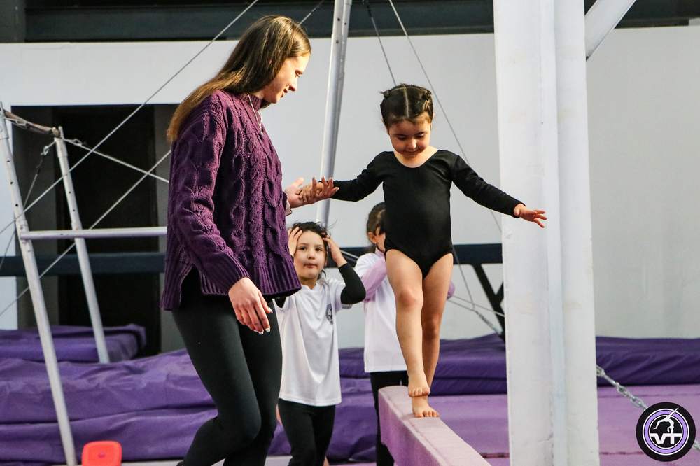 Profesora acompañando a una alumna sobre la viga de equilibrio